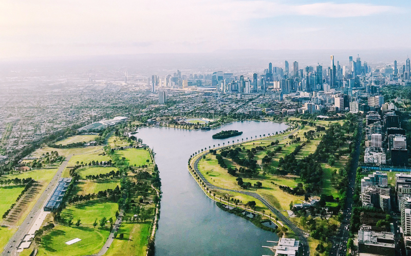 Aerial view of Melbourne city skyline with Albert Park Lake in the foreground, highlighting the vibrant urban landscape and green spaces.