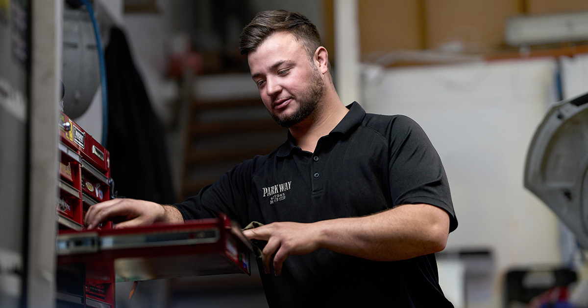 Donovan Le Roux reaching for tools in a workshop at Parkway Motors, standing beside a red tool chest in a professional garage.