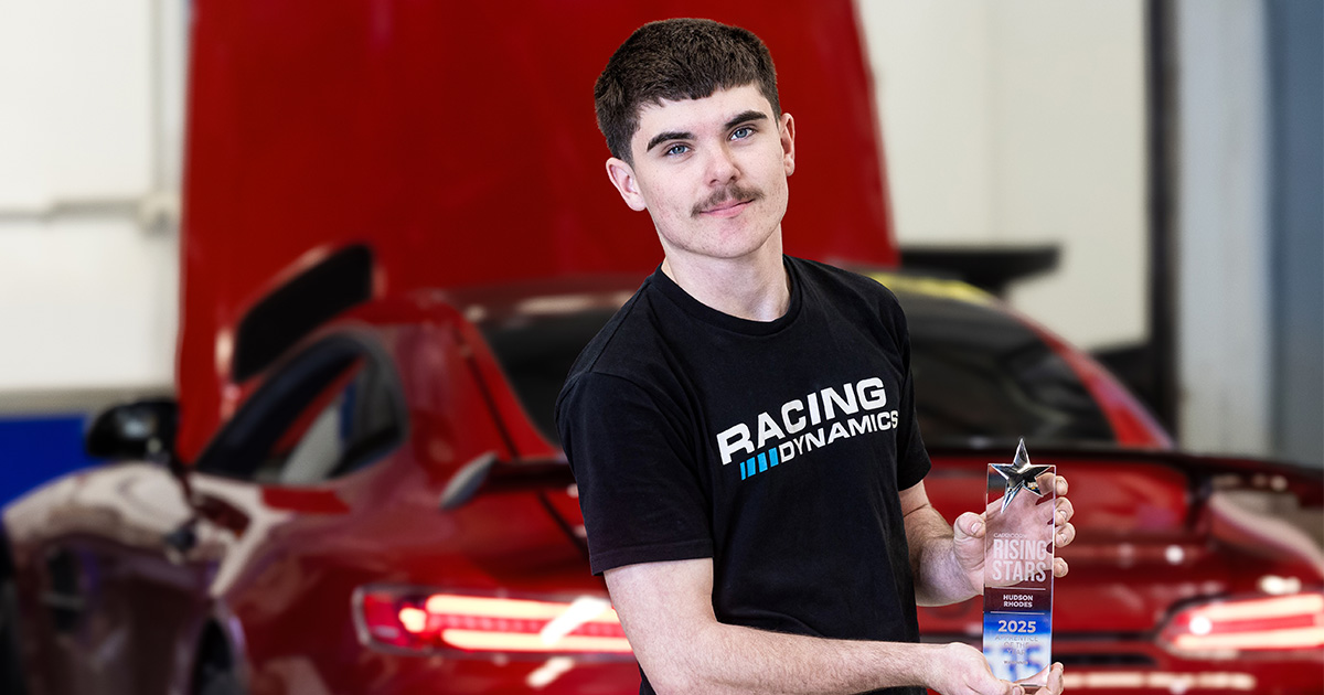 2025 Capricorn Rising Stars WA Winner, Hudson Rhodes, wearing a Racing Dynamics t-shirt holding his trophy while standing in front of a red high-performance sports car with its bonnet open inside a workshop