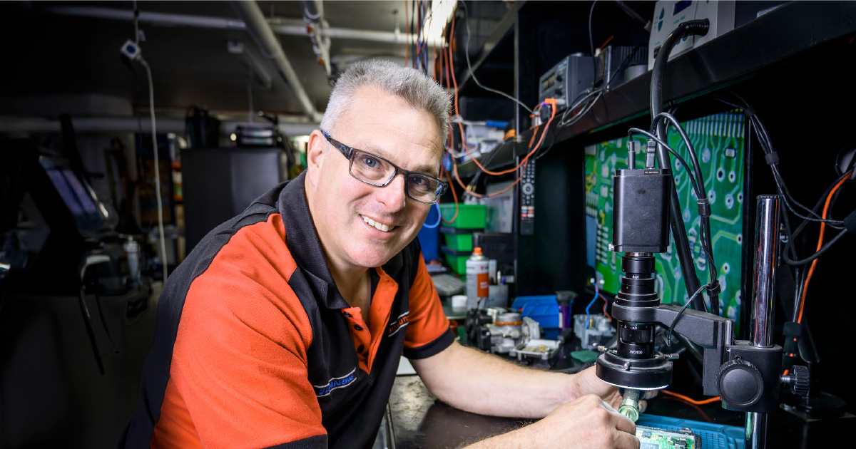 Capricorn Member using a microscope to inspect electronic components in a well-equipped automotive workshop