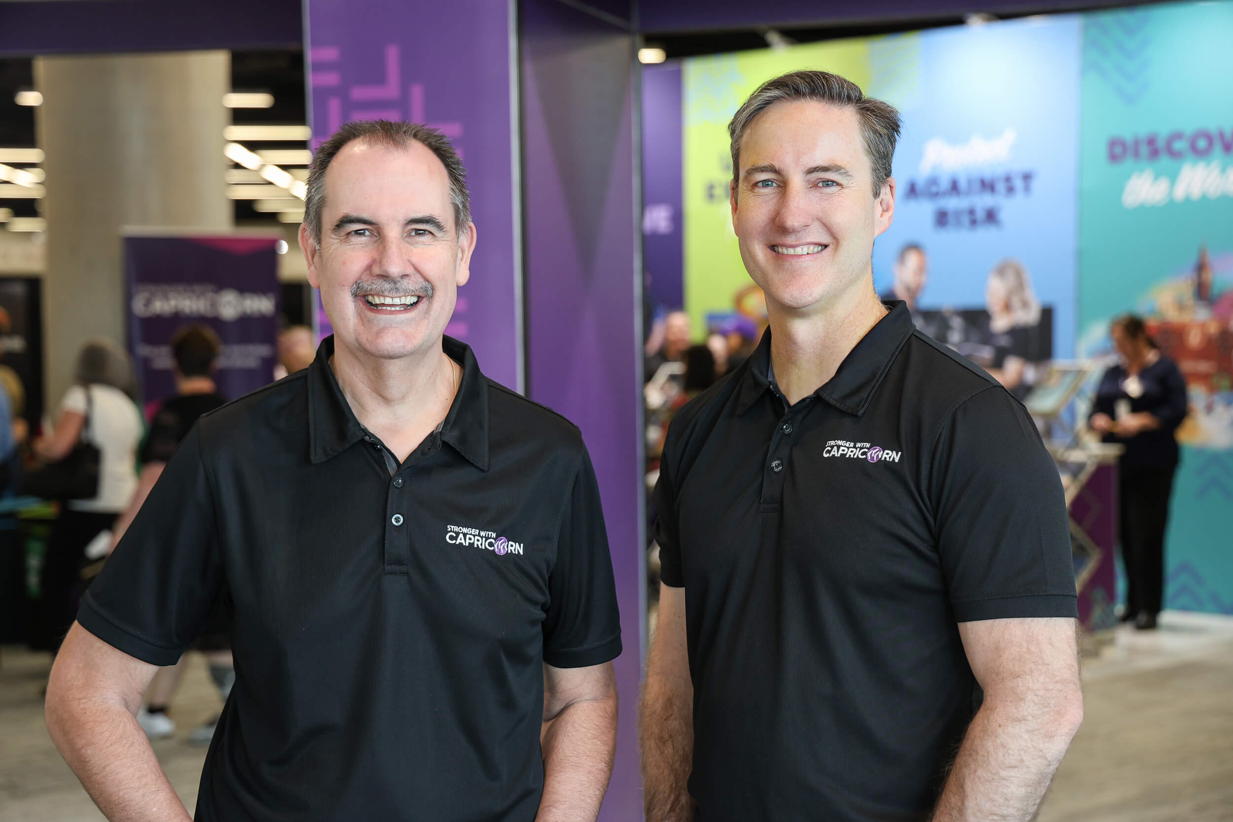 David and Brad standing at a trade show smiling at the camera in Capricorn polo shirts